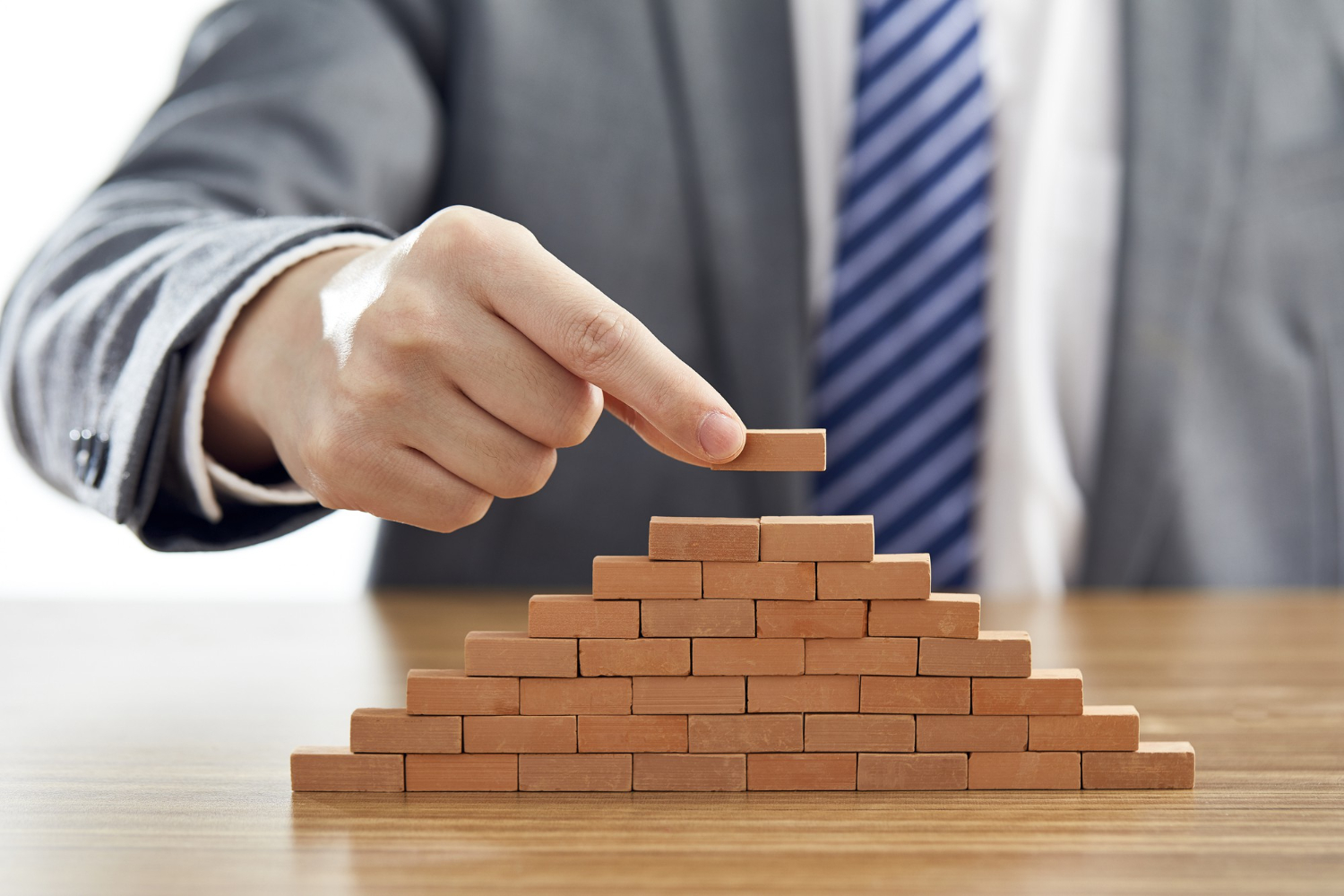 businessman-suit-putting-last-piece-pyramid-using-wooden-blocks