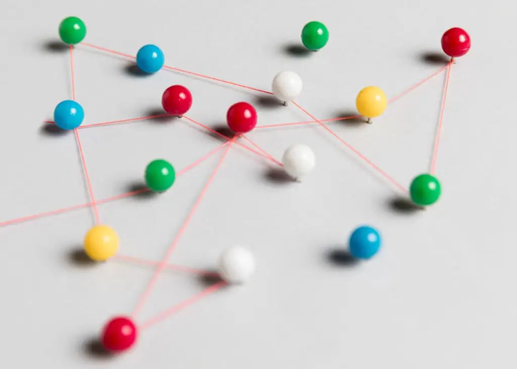 Colored map pins joined by red string on a white surface